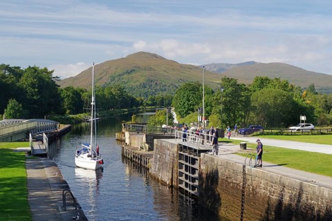 A sailing boat in the canal surrounded by green trees and mountains on a clear day, Caledonian