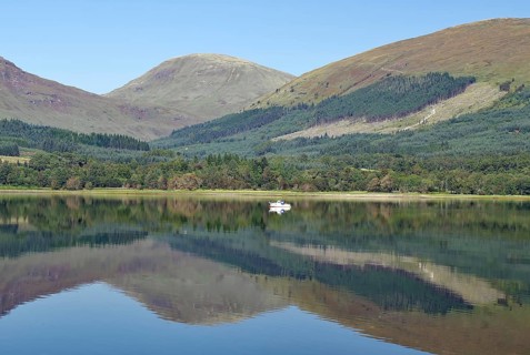 A boat on a glassy loch surrounded by mountains under a clear sky, Loch Eil, Scotland, Great