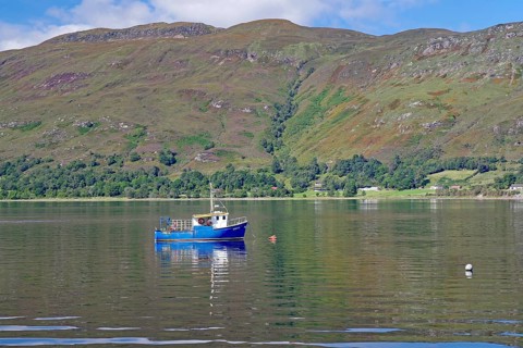 Small boat floating on a calm lake surrounded by green mountains, Fort William, Scotland, United