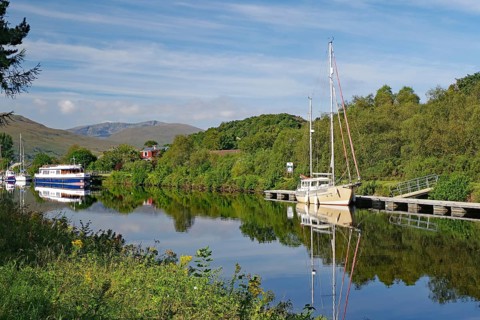 River landscape with boats and wooded hills in the background, Caledonian Canal, Fort William,