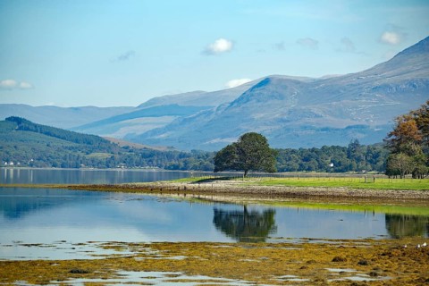 A tranquil loch surrounded by mountains with a peaceful natural landscape in the background, Loch