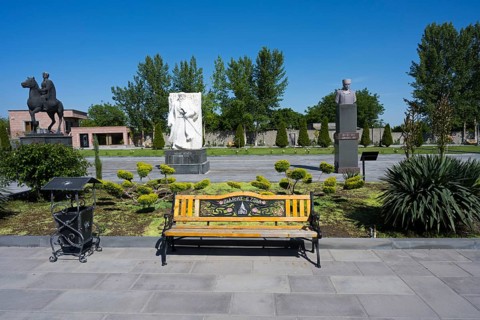Park with colourful wooden benches, statues and surrounding trees, in the garden of the Yazidi
