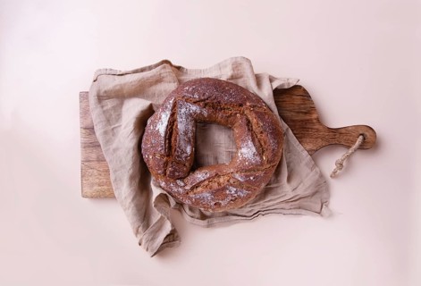 Round handmade rye bread on wooden board with linen napkin, on beige background top view, copy