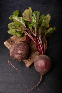 Beetroot with tops lies on a wooden board on a dark background, selective focus