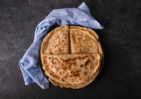 Appetizing pancakes with filling on a plate with a blue napkin, on a black background, space for