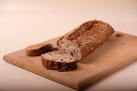 Slices of whole grain bread with carrots and seeds on wooden board on beige background, copy space