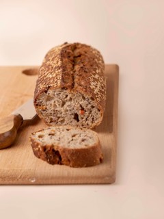 Whole grain bread with carrots and seeds on wooden board on beige background, copy space
