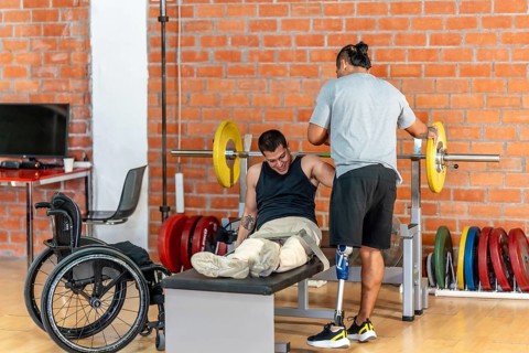 Man with prosthetic leg spotting another man with leg injuries or absence, who struggles with a