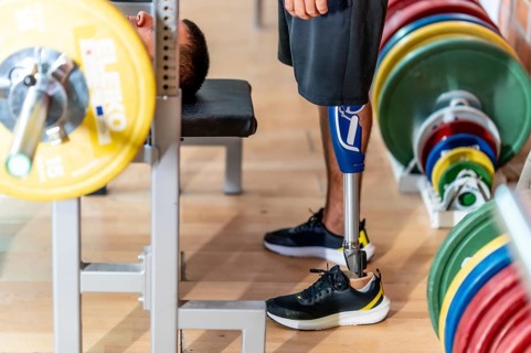 Adaptive athlete with a prosthetic leg doing weightlifting exercises on a gym bench, demonstrating