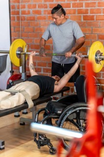 Adaptive athlete in a wheelchair performing bench press exercises with a spotter at the gym,