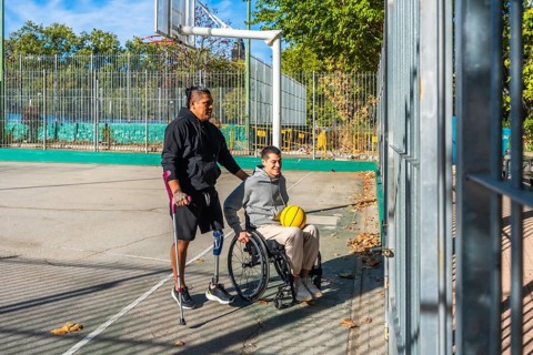 Friends celebrating sports inclusion on a sunny outdoor basketball court, one man with crutches and