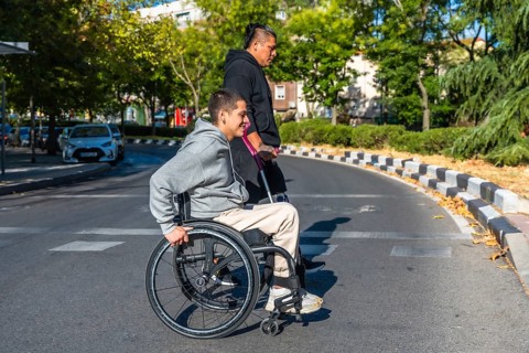 Two diverse young individuals with disabilities walking on a city road, one person using a