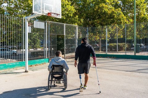 Two young men, one in a wheelchair and the other with a prosthetic leg, are walking together