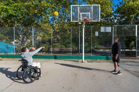 Two young men, one using a wheelchair and another with a prosthetic leg, playing basketball on an