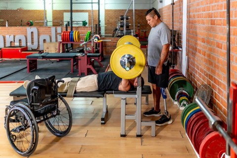 Two determined men training in a gymone bench pressing weights while his teammate with a prosthetic