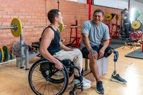 Two disabled men, one using a wheelchair and the other with a prosthetic leg, smiling while