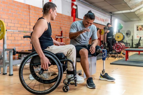 Two young men with disabilities one in a wheelchair, one with a prosthetic leg laughing and bonding
