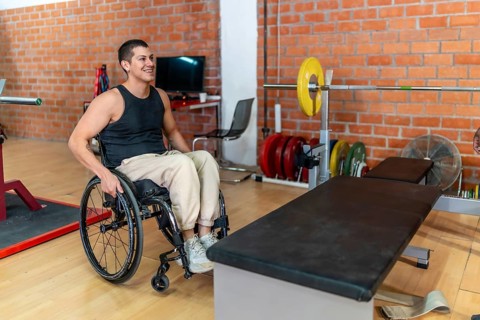 Young man in a wheelchair preparing for a workout next to a weightlifting bench and barbell at an
