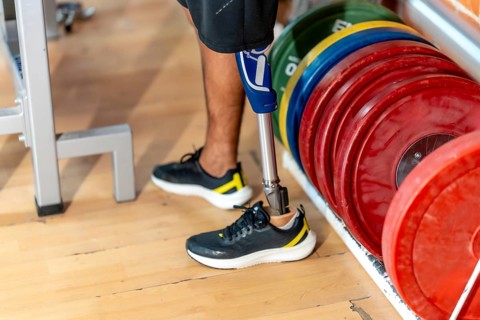 Amputee man standing on a wooden floor in a gym, wearing a modern prosthetic leg and a normal shoe