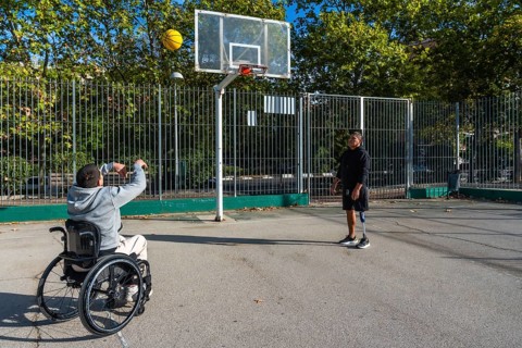 Two disabled friends are enjoying a game of basketball on an outdoor court, with one man in a