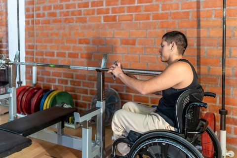 Young man in a wheelchair setting up a barbell in a modern gym, focused and determined as he trains