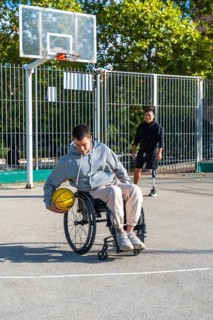 Young men with physical disabilities engaging in adaptive basketball. One person using a wheelchair