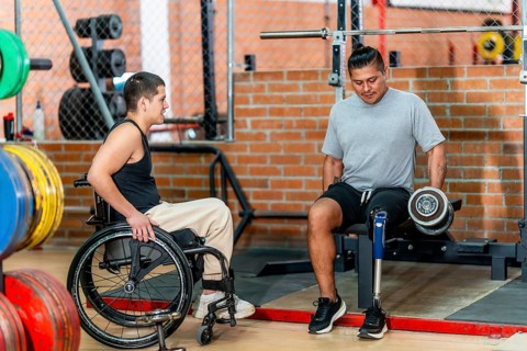 Two men with disabilities, one using a wheelchair and another with a prosthetic leg, engaging in