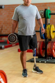 Disabled man with prosthetic leg lifting a dumbbell in gym, focused on strength training and