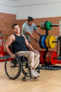 Disabled man in a wheelchair looking cheerful and smiling at the camera while another man with a