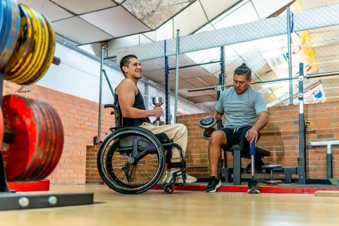 Two men with disabilities training together in a gymone in a wheelchair, one with a prosthetic