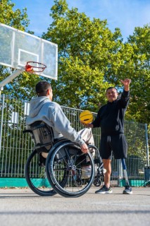 Smiling men with physical disabilities engaging in a friendly game of basketball on an outdoor