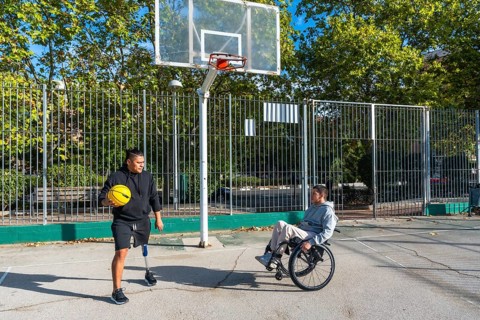 Disabled men, one using a wheelchair and the other wearing a prosthetic leg, playing basketball on