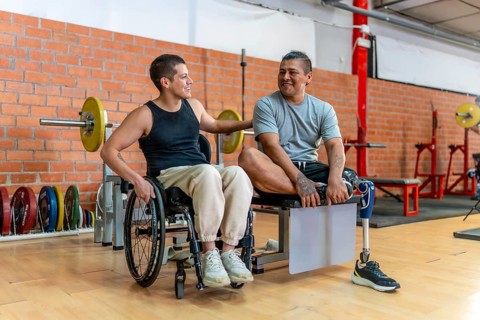 Two adaptive athletes, one in a wheelchair and one with a prosthetic leg, smiling and supporting
