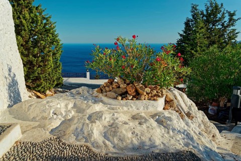 Sunny square with blooming oleander, surrounded by white rocks and views of the blue sea, Church of