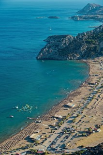 View of the sunny coastal landscape of Tsambika with sandy beach, blue sea and cliffs, Church of