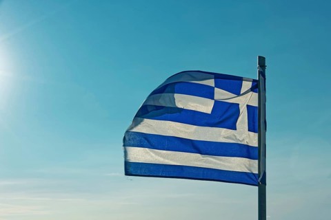 The Greek flag flies in the wind against a clear blue sky with sunshine, Church of the Virgin Mary