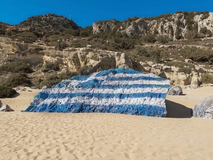 Rock painted with a Greek flag on the sandy Tsambika beach under a clear sky, Tsambika beach,