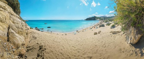 A quiet place on Tsambika sandy beach of Tsambika with clear blue sea and rocks under a sunny sky,