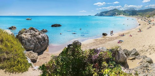Picturesque Tsambika bay with clear water, rocks and sandy beach. People enjoying the sun, a boat