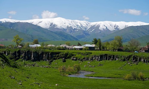A village in a green landscape with snow-capped mountains in the background, Saratovka, Lesser