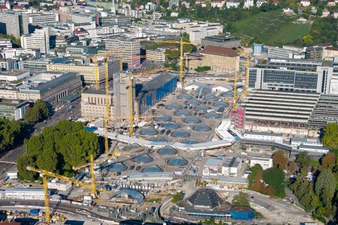 Panoramic view of modern construction site with glass structures and cranes in an urban green area,