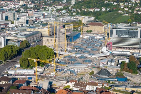 Urban construction project with glass structures and cranes, embedded in a green urban backdrop,