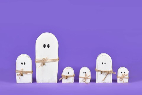 Cute wooden white Halloween ghost ornaments in a row on purple background