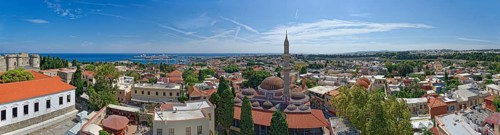 A sweeping panoramic view of the old town of Rhodes with a minaret and the sea in the distance,