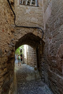 Cobbled alley with arched passageway and stone walls, a man in the background, Medieval town of