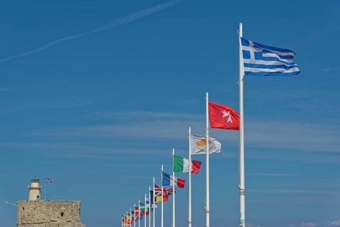 Several flags waving in the wind against a clear blue sky, including the Greek flag, Mandraki