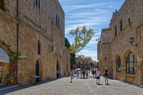 Historic old town street with cobblestones and old buildings under a blue sky full of tourists,