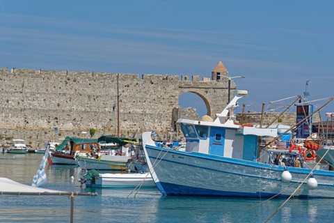 Fishing boats lying in the calm water in front of a historic city wall, Mandraki harbour, Medieval
