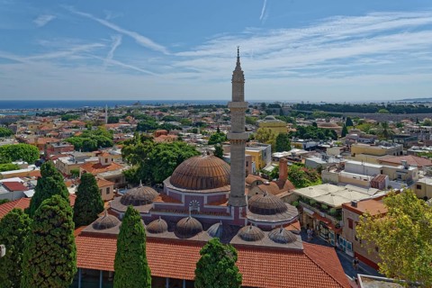 A panoramic view with minaret and domes in front of a cityscape of Rhodes and the sea in the