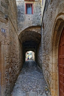 Narrow stone-paved alley with arches and high stone walls, quiet atmosphere, Medieval Town of